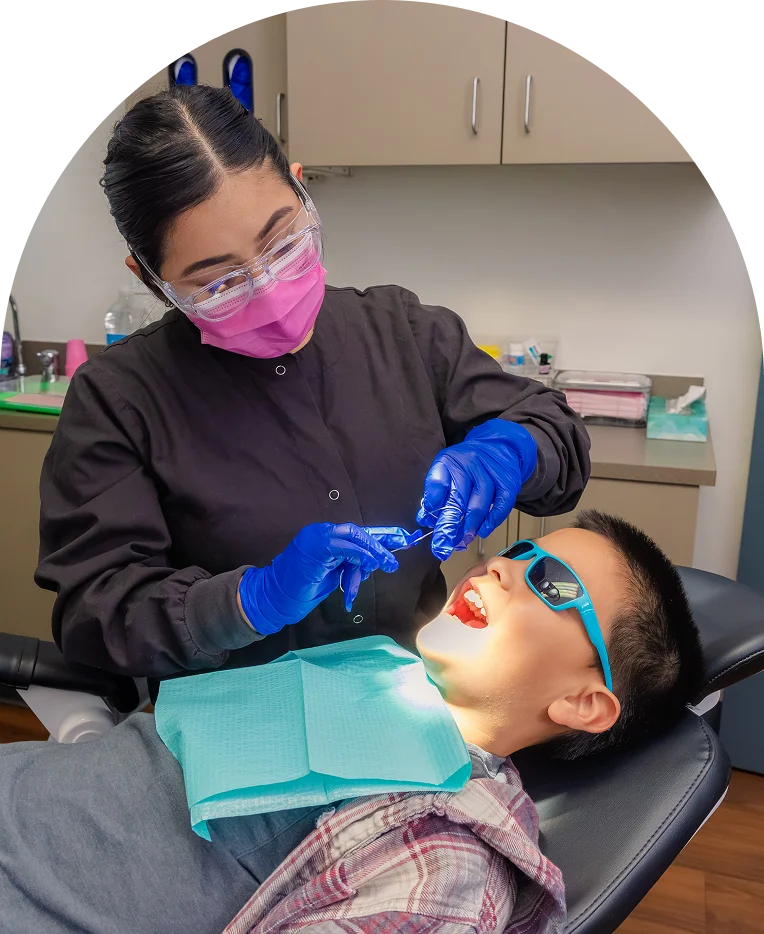 Dental assistant treating a young patient in sunglasses at Pleasant Valley Pediatric Dentistry